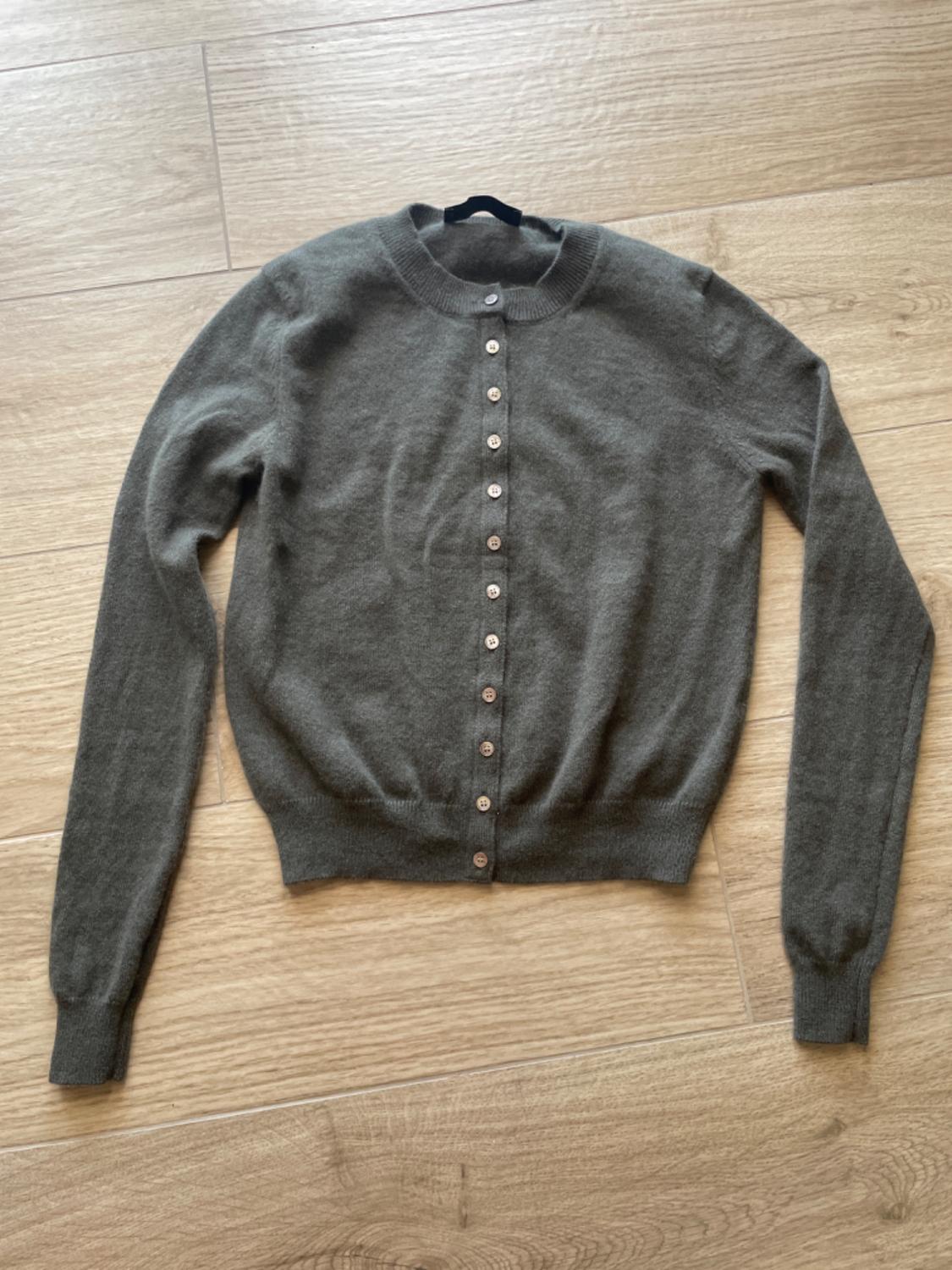 Dark grey knitted cardigan with a round neck and buttons, long sleeves. Casual style, laid out on a light wood floor.
