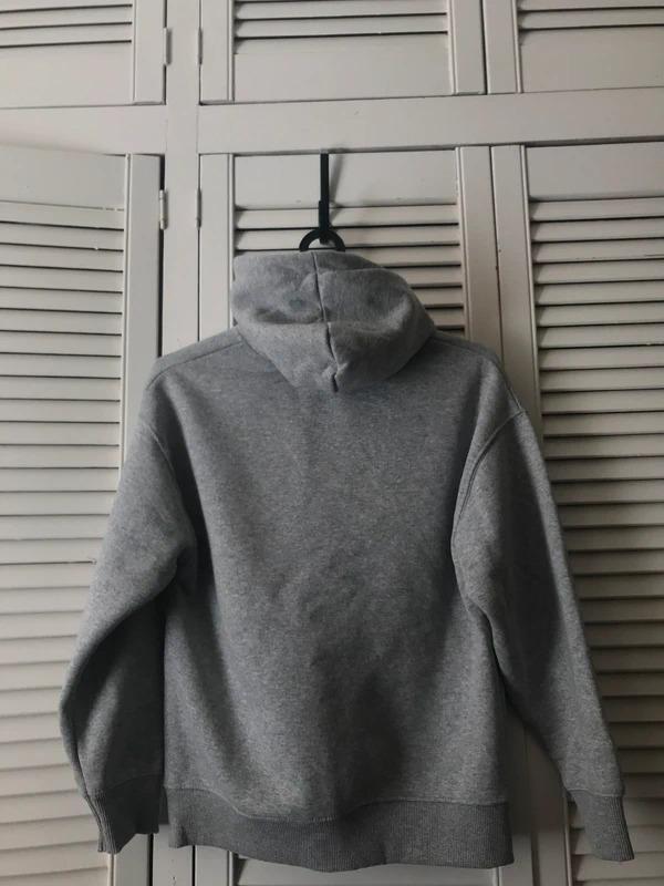 Grey hooded sweatshirt hanging on a black coat hanger in front of white shuttered wardrobe doors.