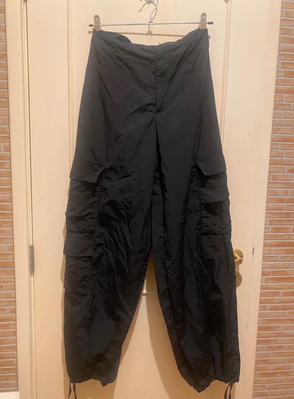 Black baggy trousers hanging on a hanger over a beige door, with side pockets and wrinkled texture.