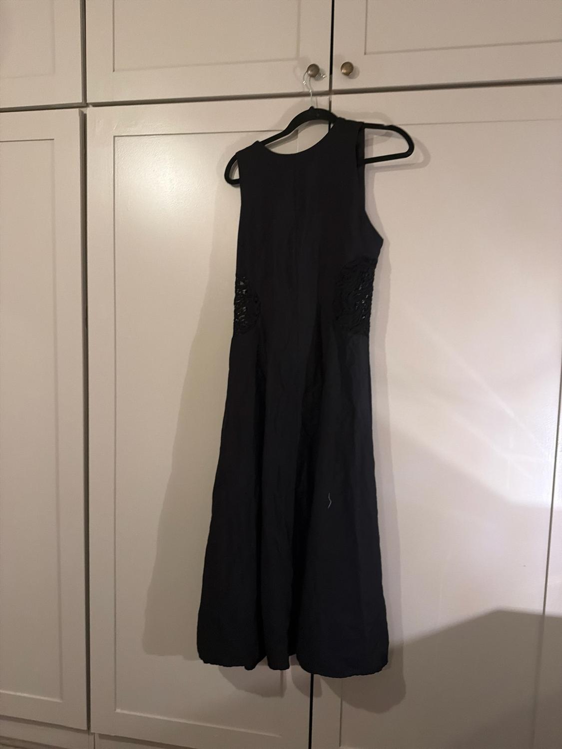 Sleeveless black dress with lace detailing at the sides, hanging from a hanger on the doors of a white wardrobe.