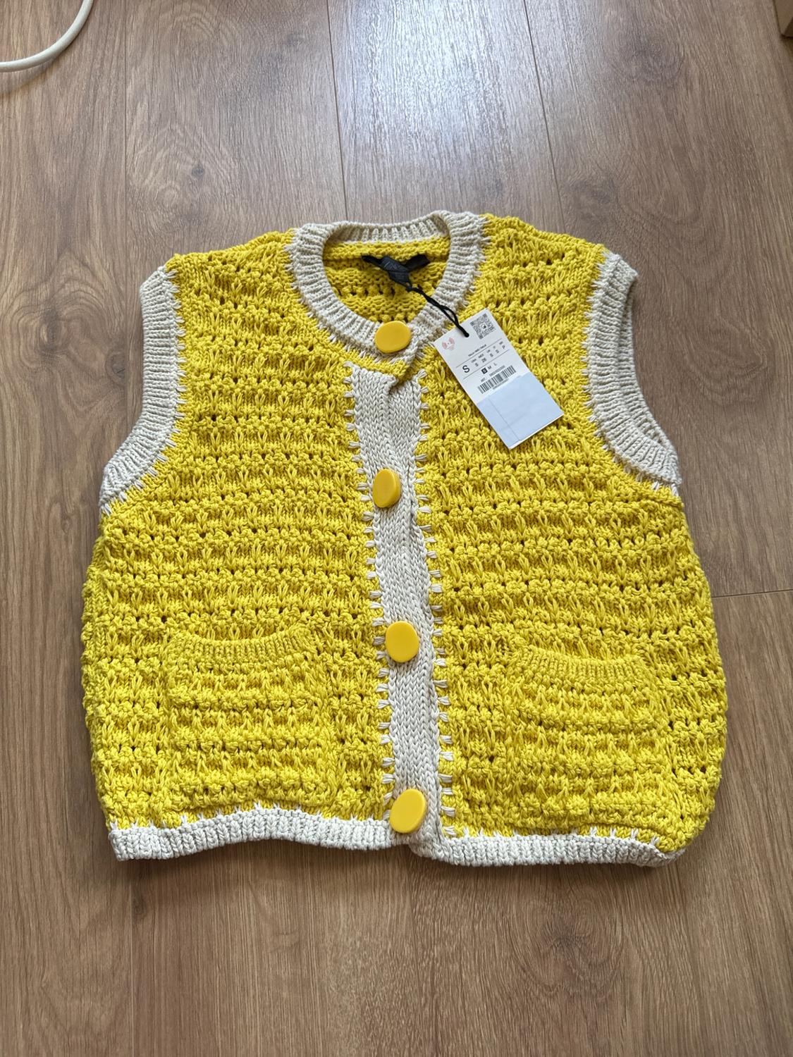 Yellow chunky knit cardigan with beige trim and large buttons, on a wooden floor.