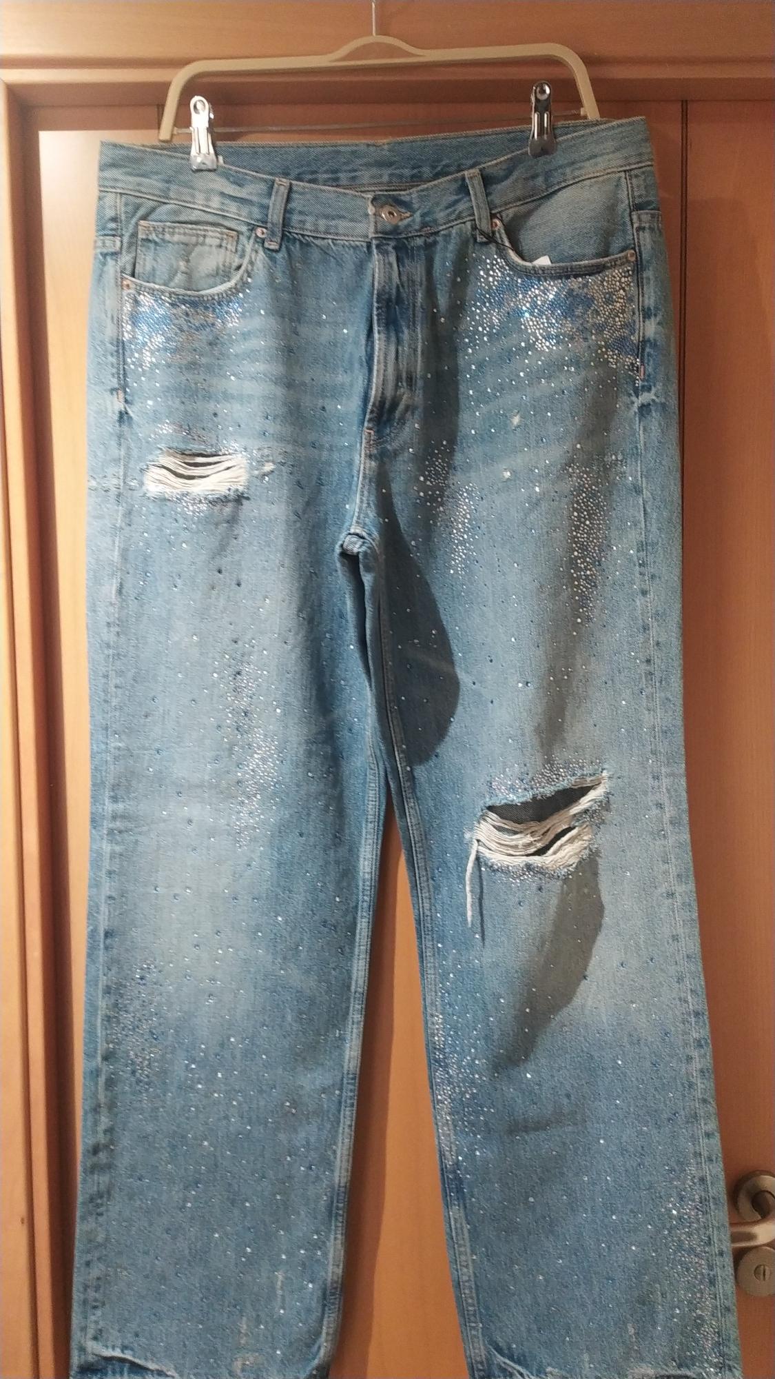 Blue jeans hanging with glitter details and rips on the legs, against a light wood background.