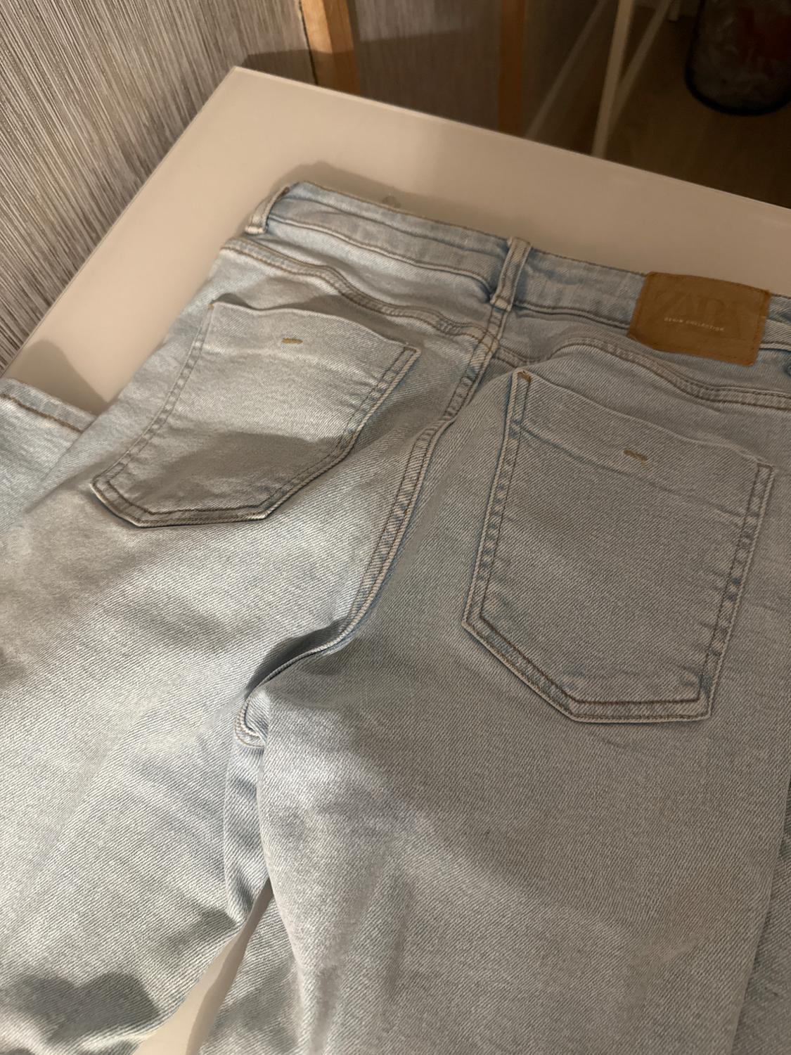 Light denim jeans on a white table, showing the back pockets and a brown label on the waistband.