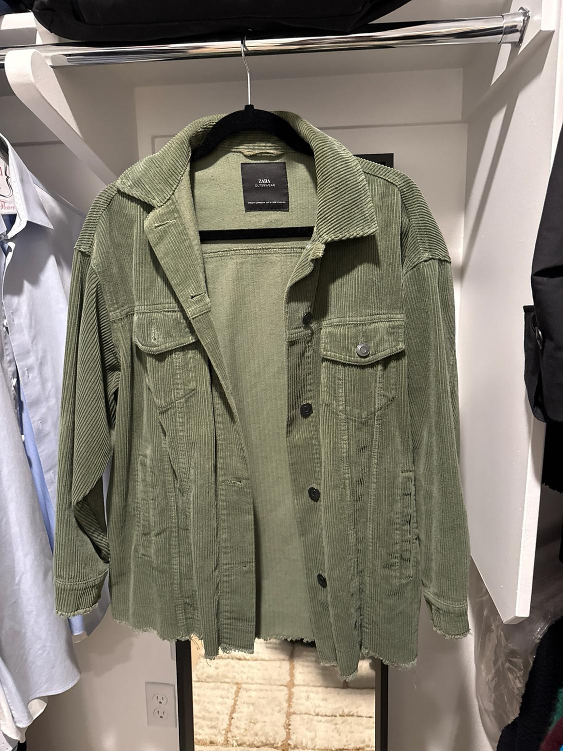 Green corduroy jacket hanging in a closet. It has buttons, pockets, and frayed cuffs. Text on the label: ZARA OUTERWEAR.