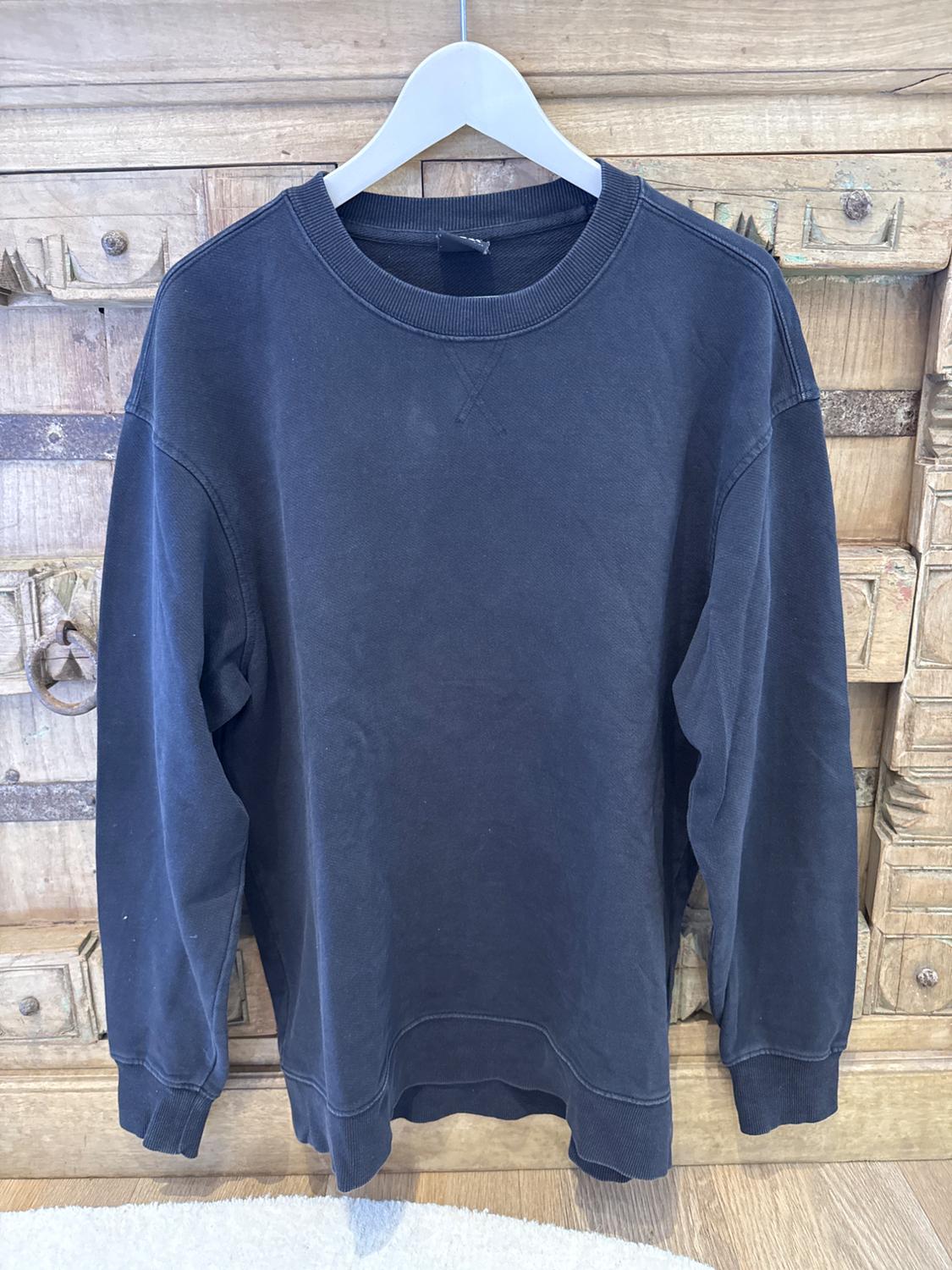 Black long-sleeved sweatshirt hanging on a white hanger, against a wooden background with carved details.