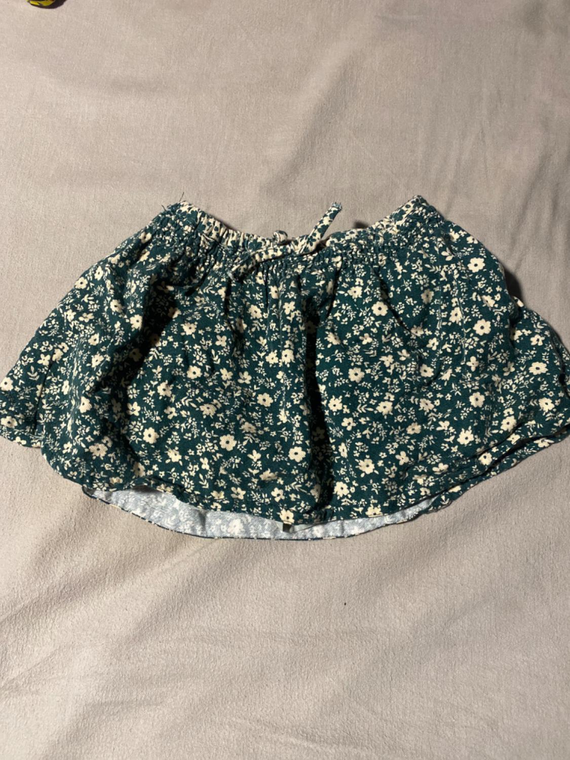 Short skirt with a white floral print on a dark green background, placed on a beige surface.