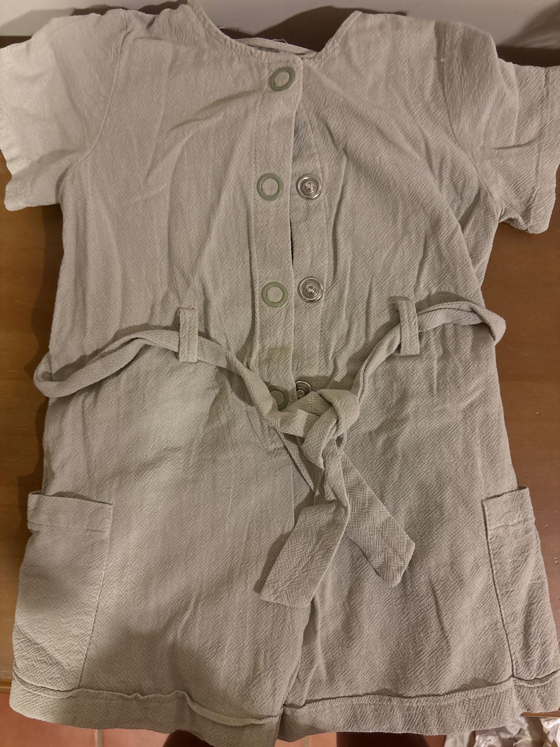 Beige textured fabric jumpsuit with front buttons and a tie belt. Short sleeves and side pockets.