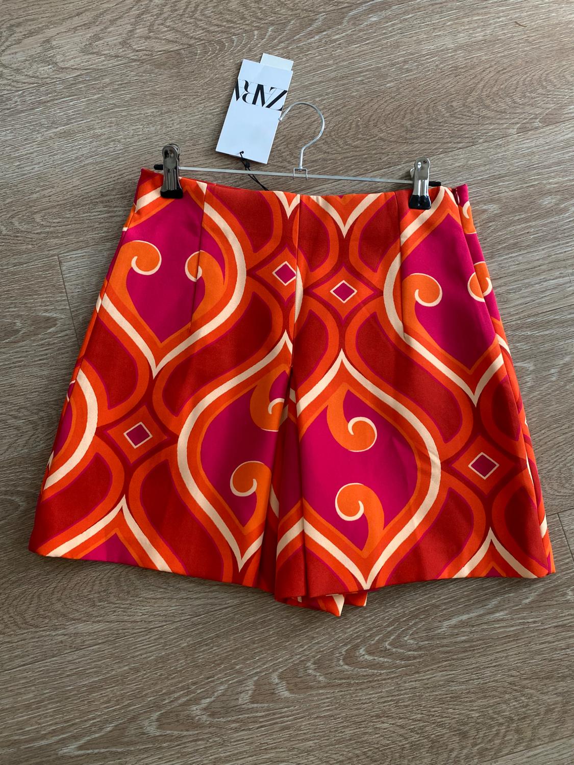 Shorts with a geometric print in orange and fuchsia tones on a wooden background. Visible label with text "ZARA".