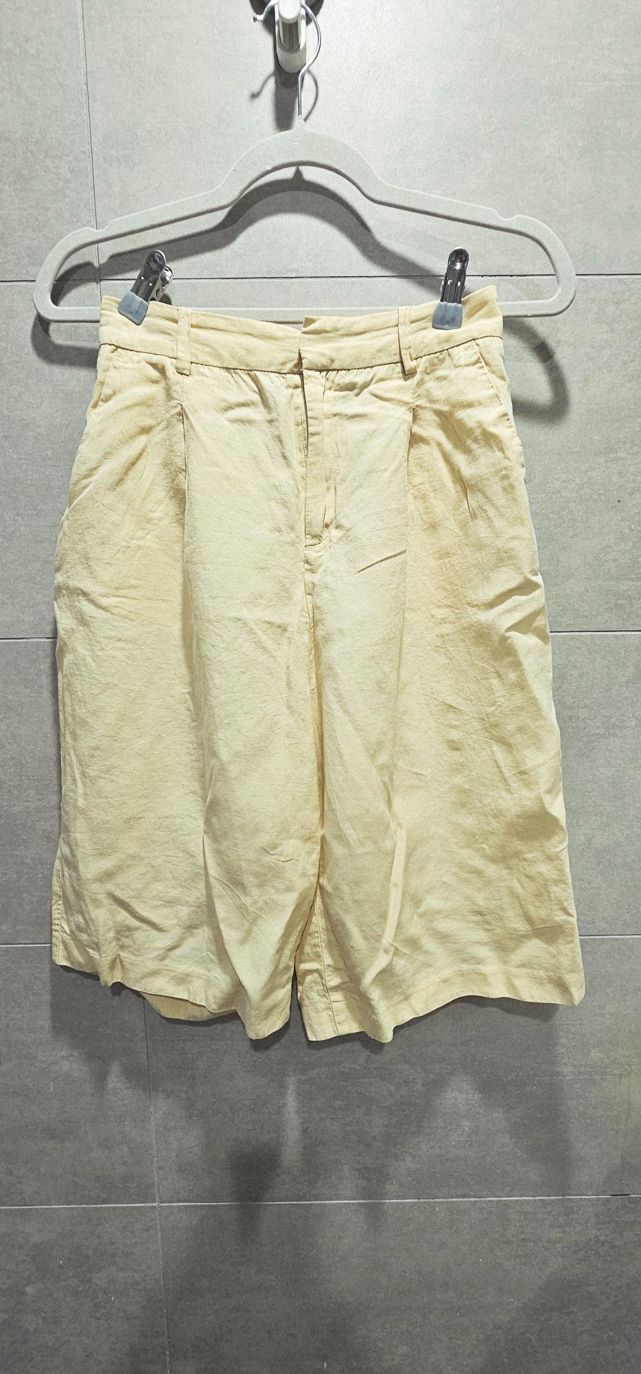 Light yellow shorts hanging on a hanger against a grey tiled wall.