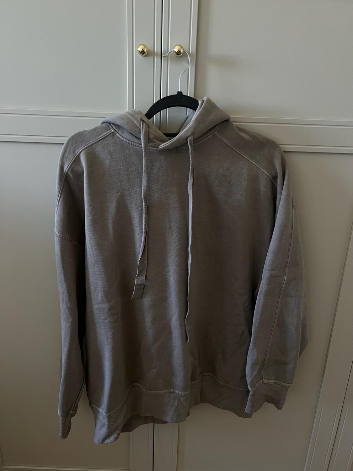 Grey hoodie hanging on a black hanger from the gold knob of a white wardrobe. Casual and relaxed style.