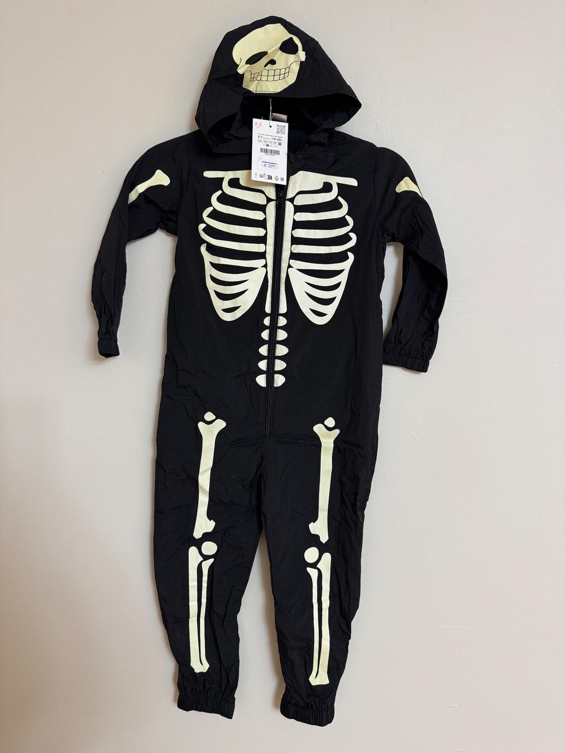 Black jumpsuit with white skeleton design and skull hood. Visible hang tag at center chest.