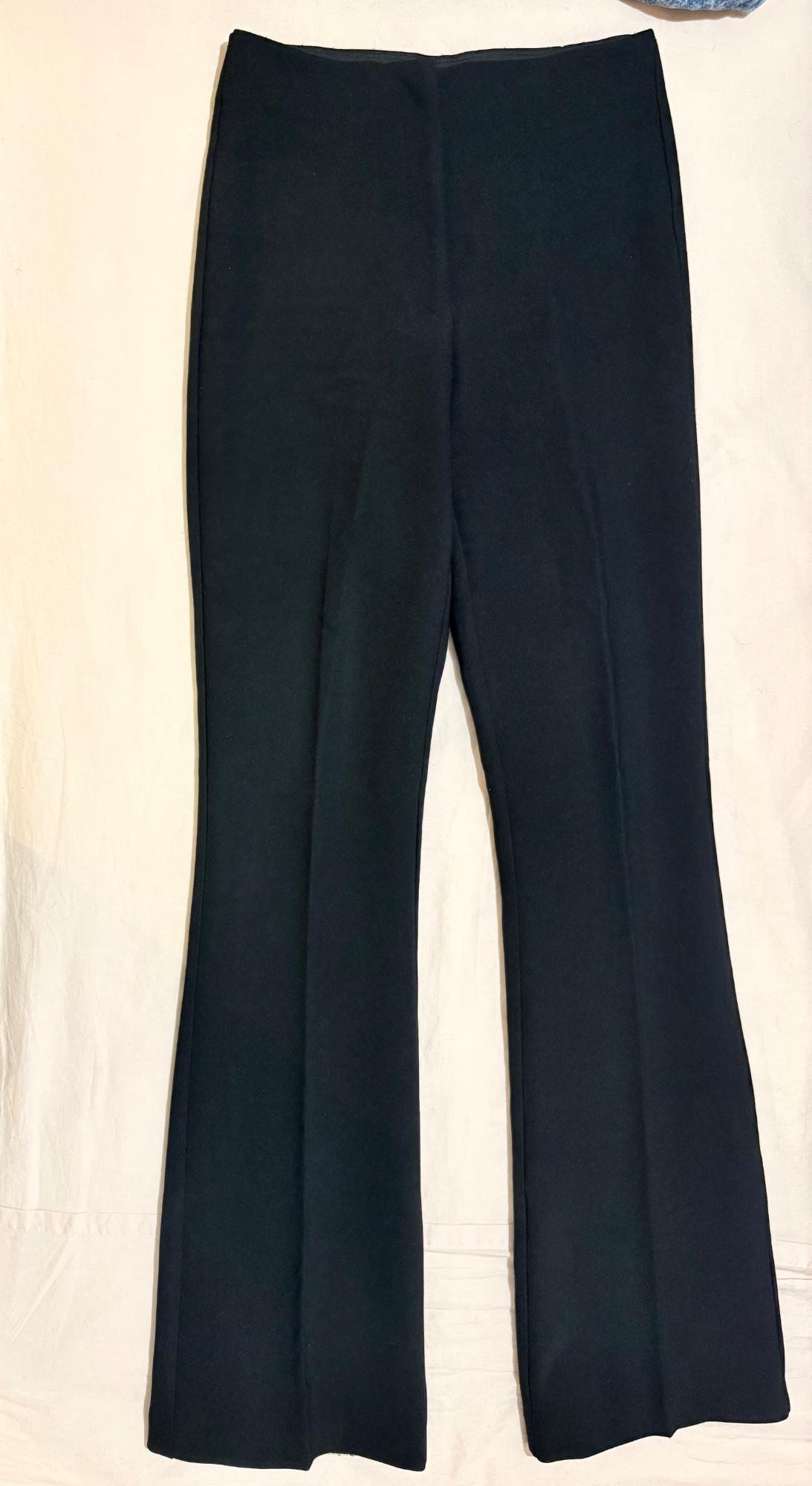 Black flared trousers with front seams, laid flat on a light-coloured fabric background.