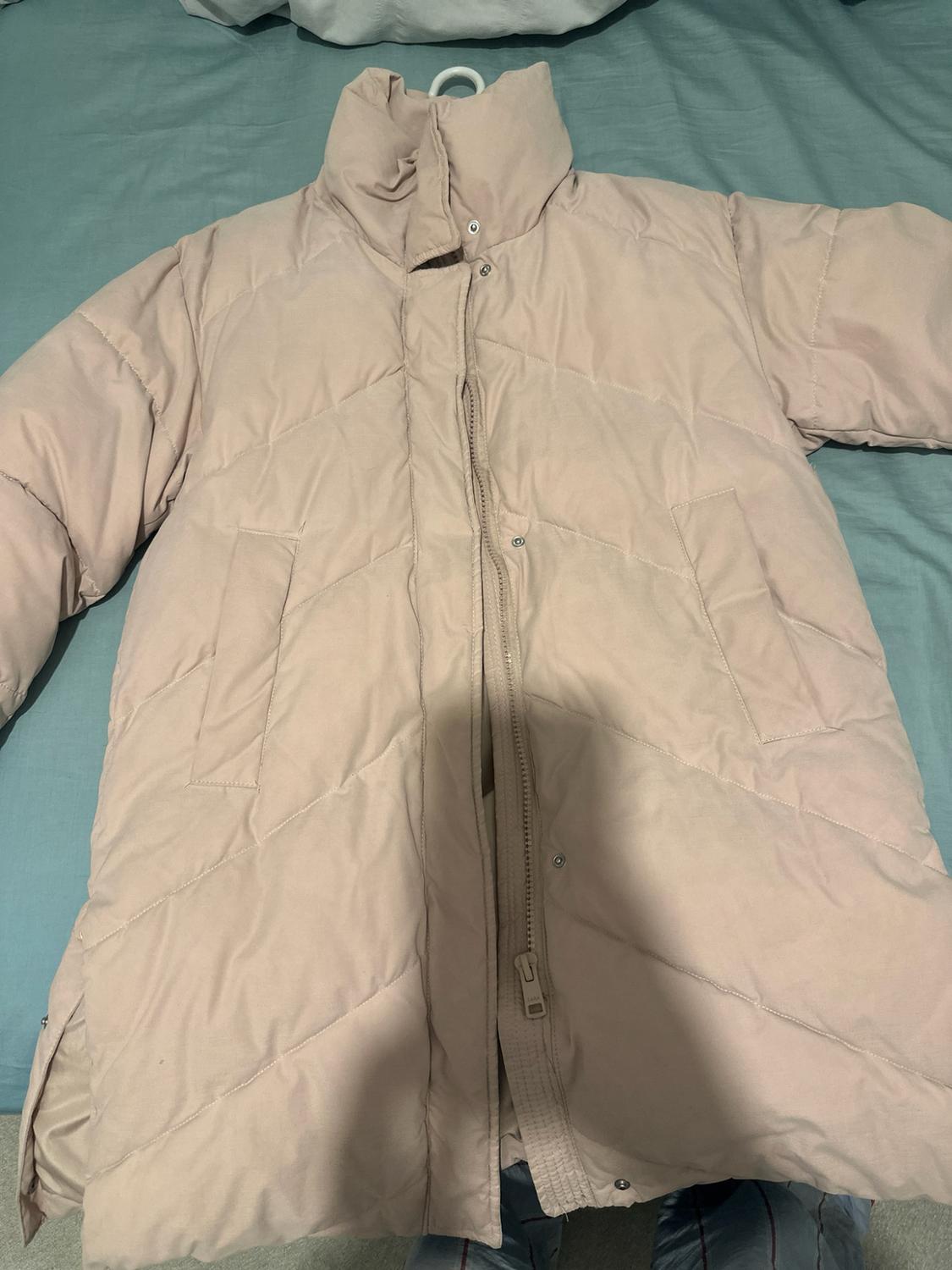 Light pink quilted coat with a high neck and pockets, laid out on blue sheets.