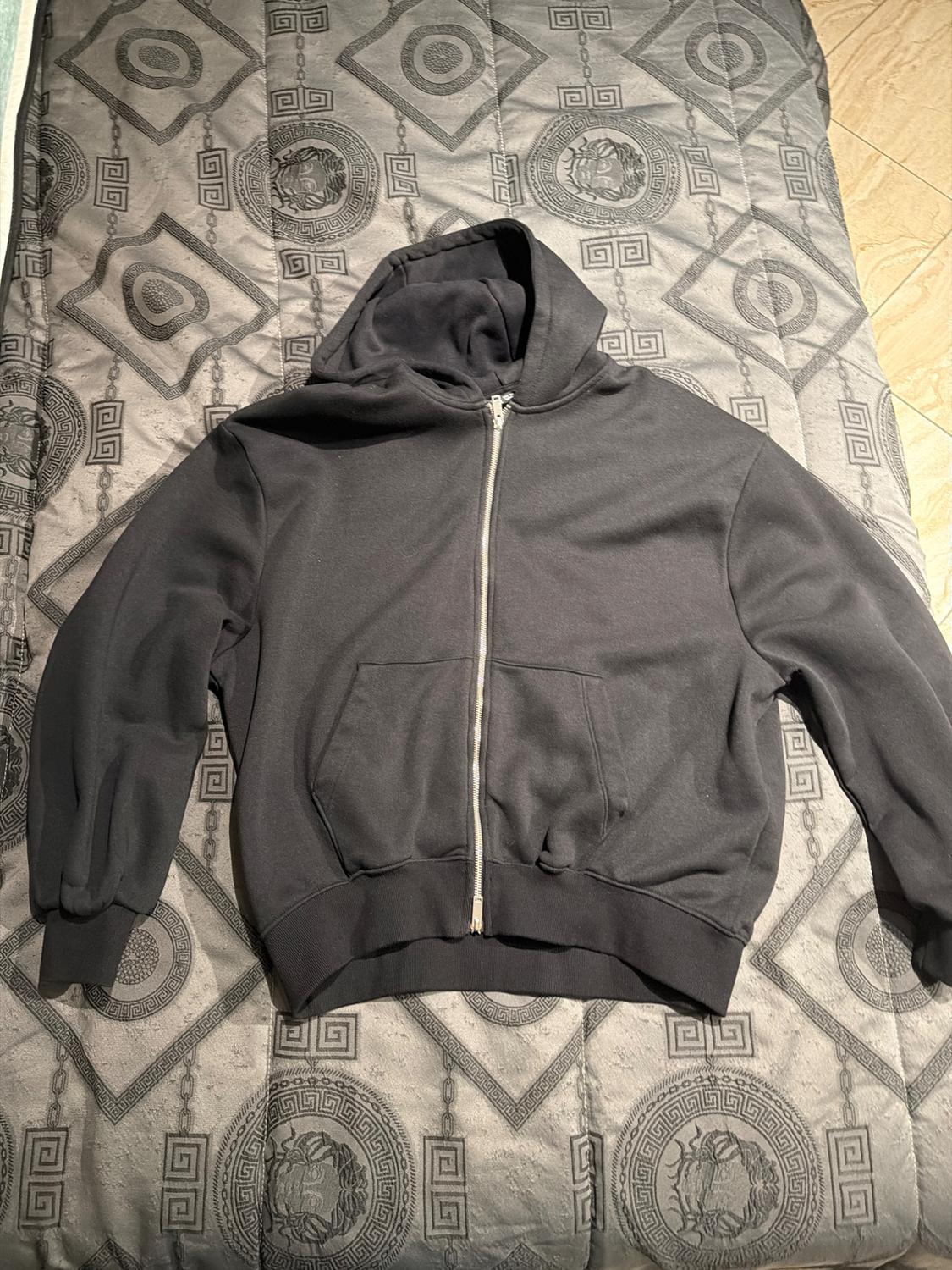 Black hooded zip-up sweatshirt on a grey quilt with geometric and lion patterns.