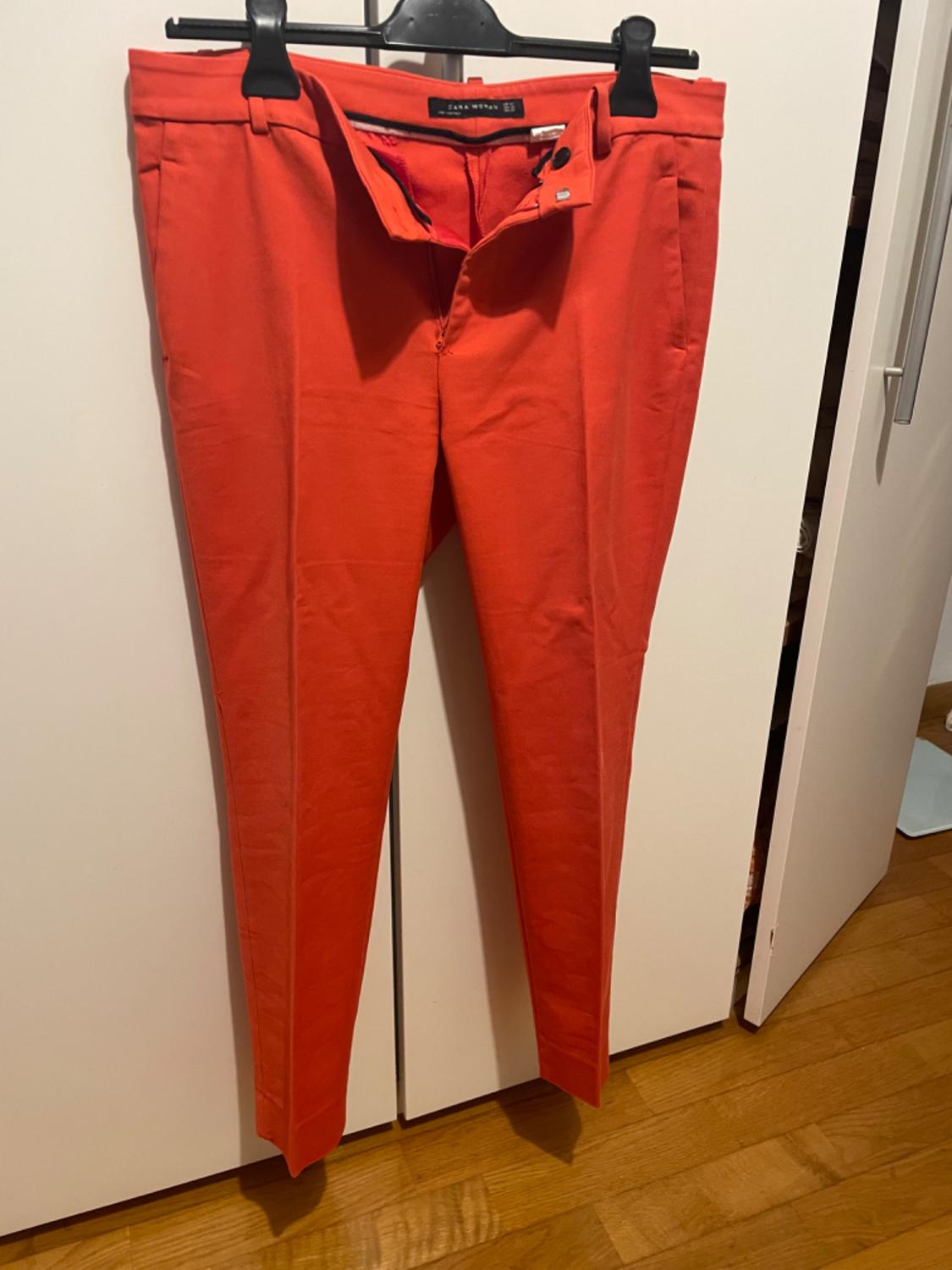 Front view of red trousers with side pockets and button and zip fastening.