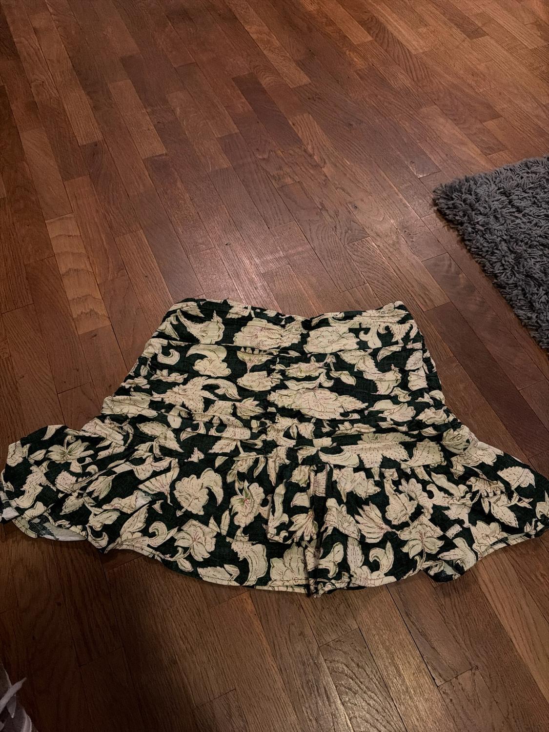 Short frilled skirt with a light floral print on a dark background, laid out on a wooden floor next to a grey rug.
