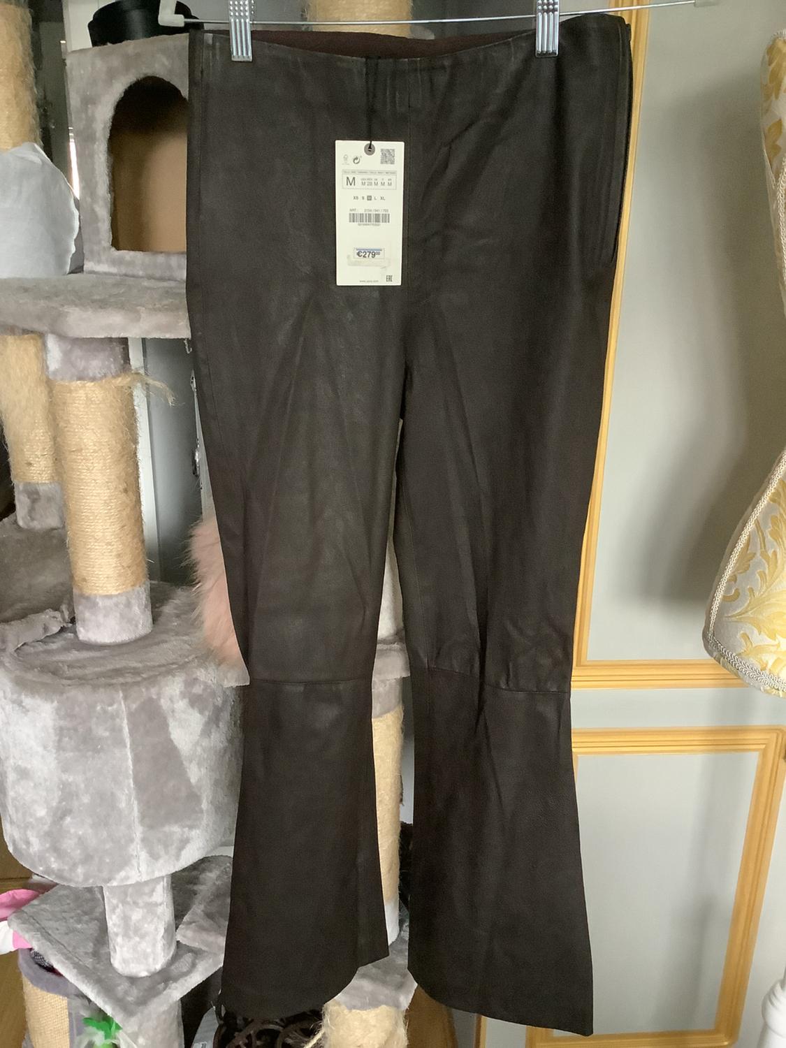 Brown trousers hanging on a clothes rail, with a visible price tag. Background with a cat scratching post structure.