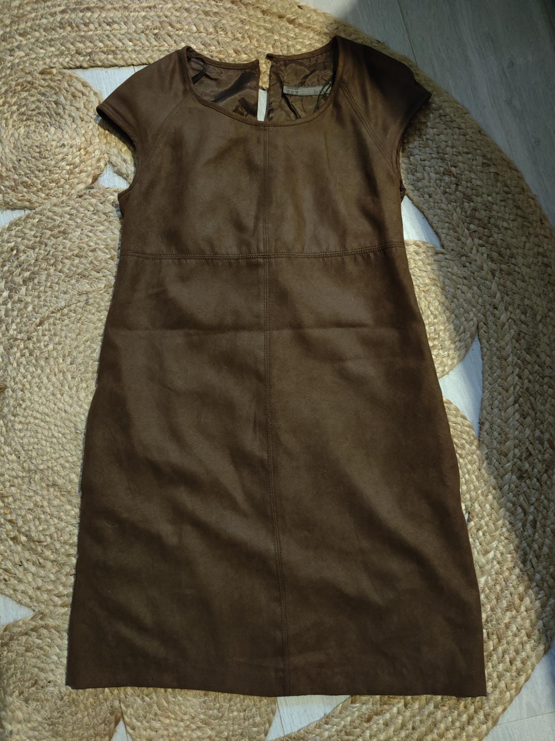 Sleeveless brown dress on a woven rug, with a simple design and a round neck, illuminated by natural light.