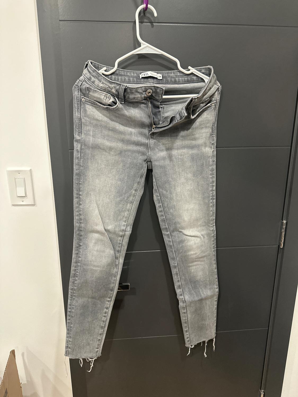 Worn grey jeans hanging on a white hanger over a dark grey door. The hems are frayed.