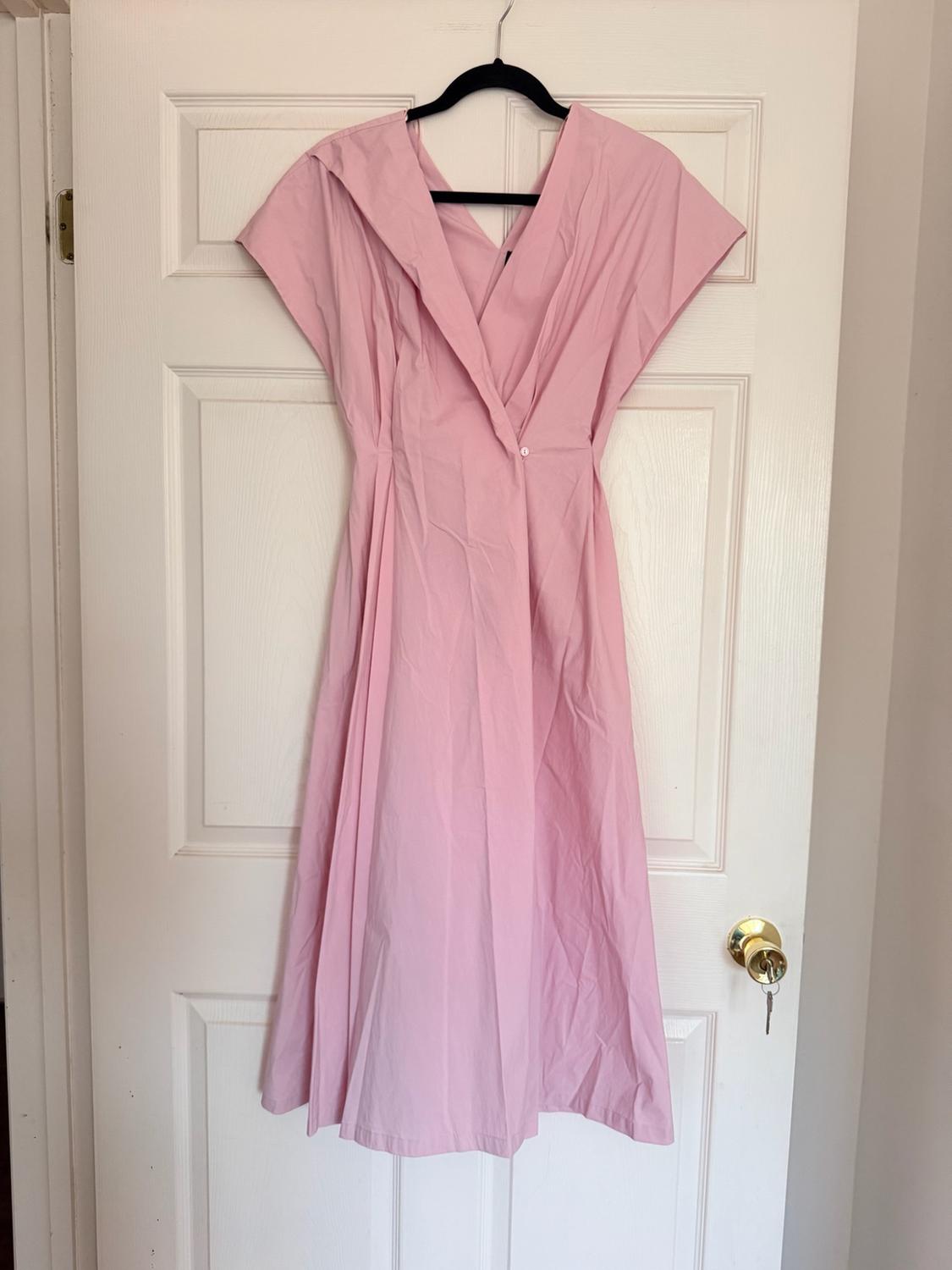 Pink short-sleeved midi dress with a wrap neckline and a button, hanging on a black hanger on a white door with a gold knob.