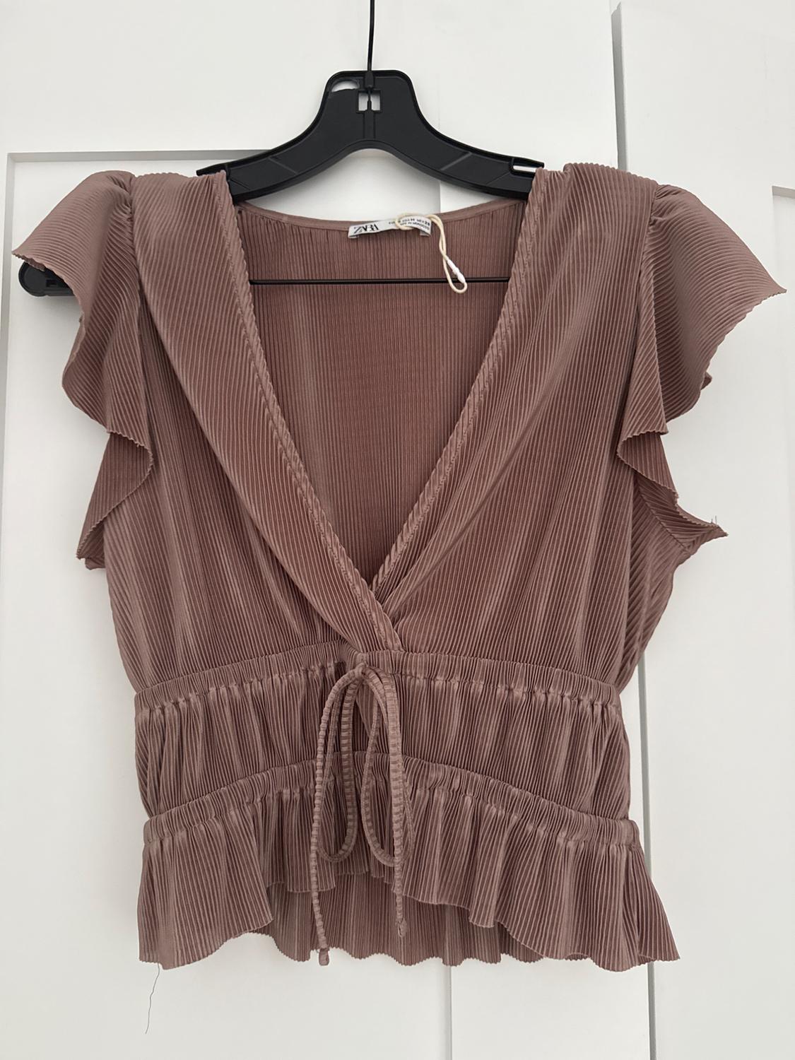 Pleated brown blouse with short ruffled sleeves, V-neck, and waist tie, hanging on a black hanger.