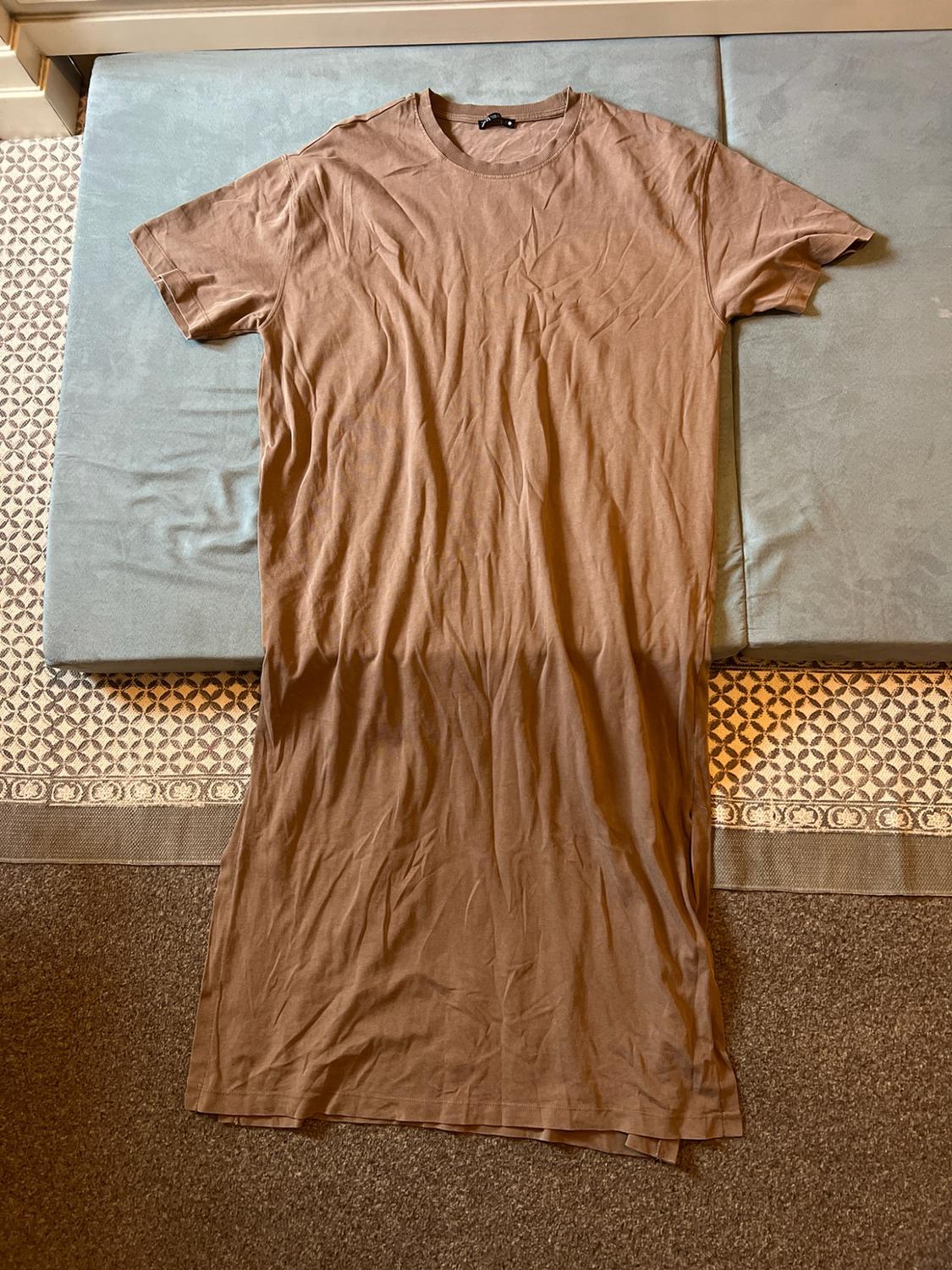 Brown short-sleeved T-shirt maxi dress, laid out casually on a blue cushion and a patterned rug.