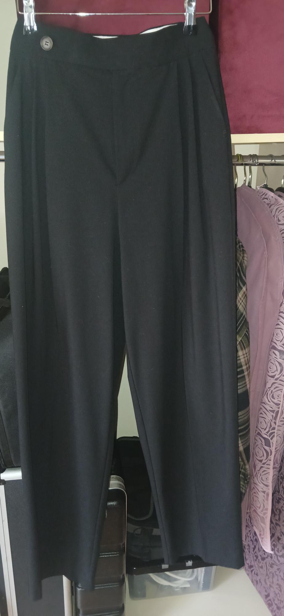 Black trousers hanging on a clothes hanger, surrounded by clothes in a wardrobe. Background with purple tones and prints.