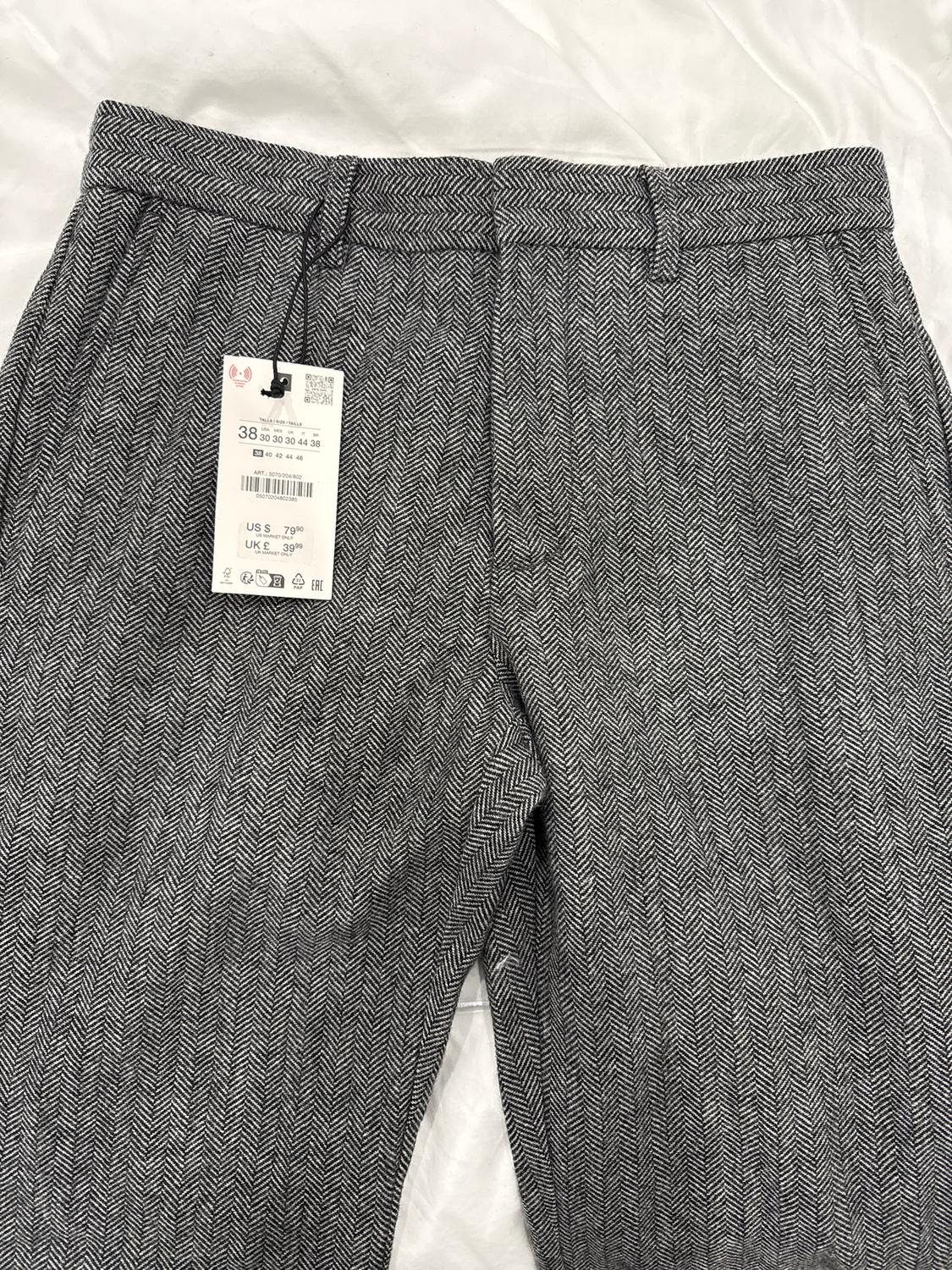 Pantalones de espiga en blanco y negro con etiqueta colgante que muestra talla 38, US 5, UK 6, sobre fondo blanco.