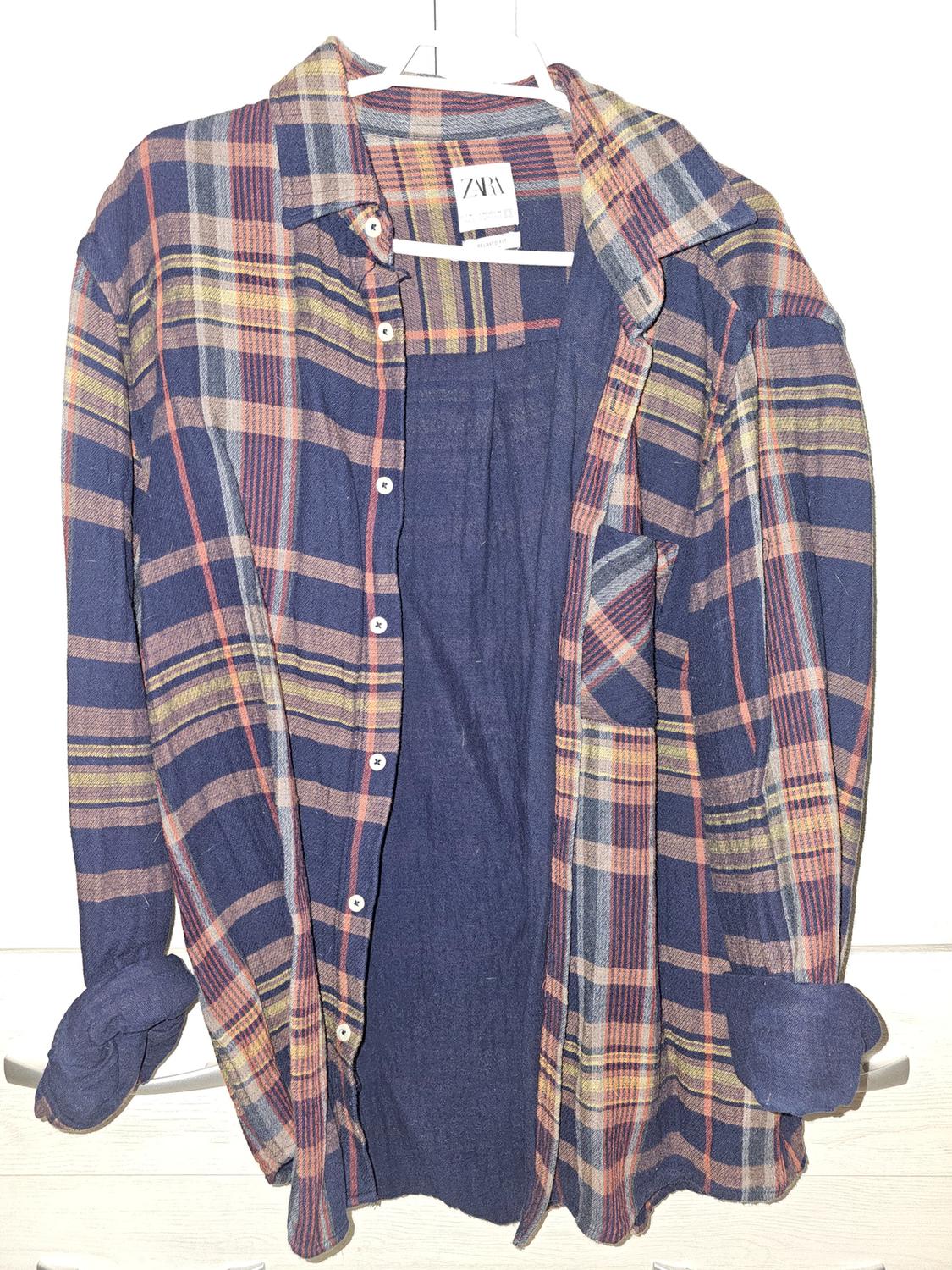 Checked shirt in shades of blue, red, and yellow, hanging on a white hanger. Visible label with the text "ZARA".