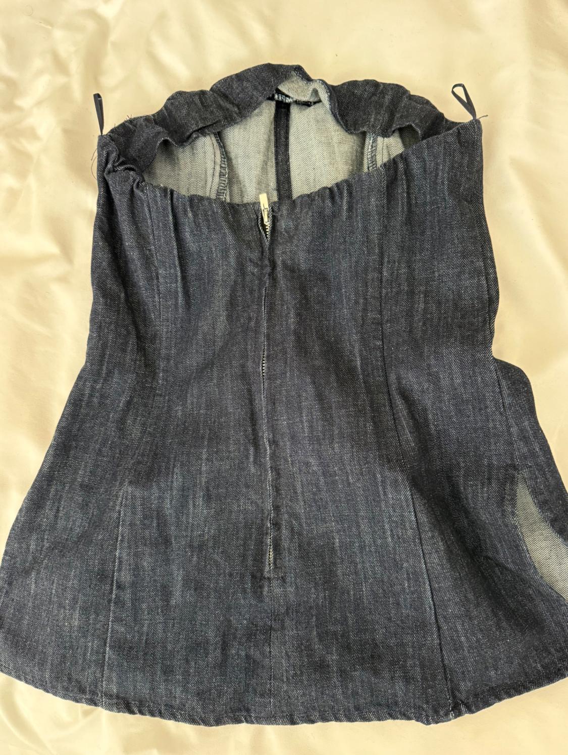 Dark blue denim zip-front top, on a beige background. Strapless design with a flared cut.