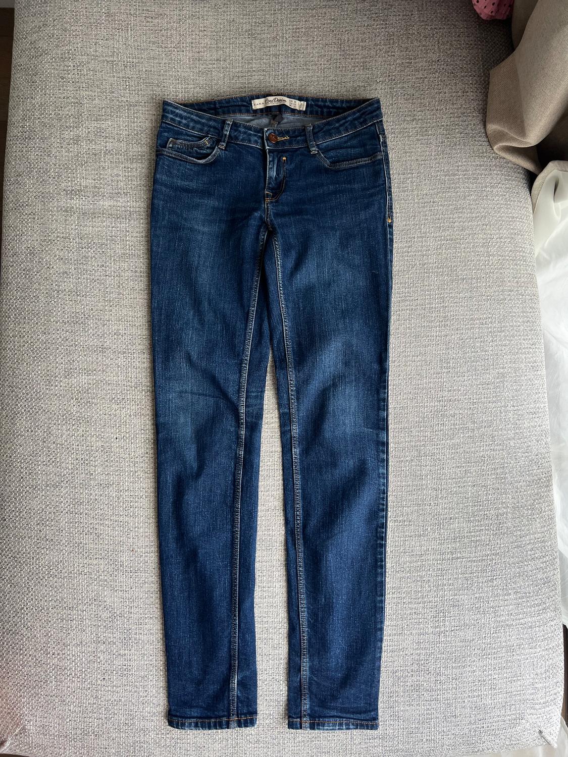 Dark blue jeans placed on a light grey sofa, with visible stitching details and a waist label.