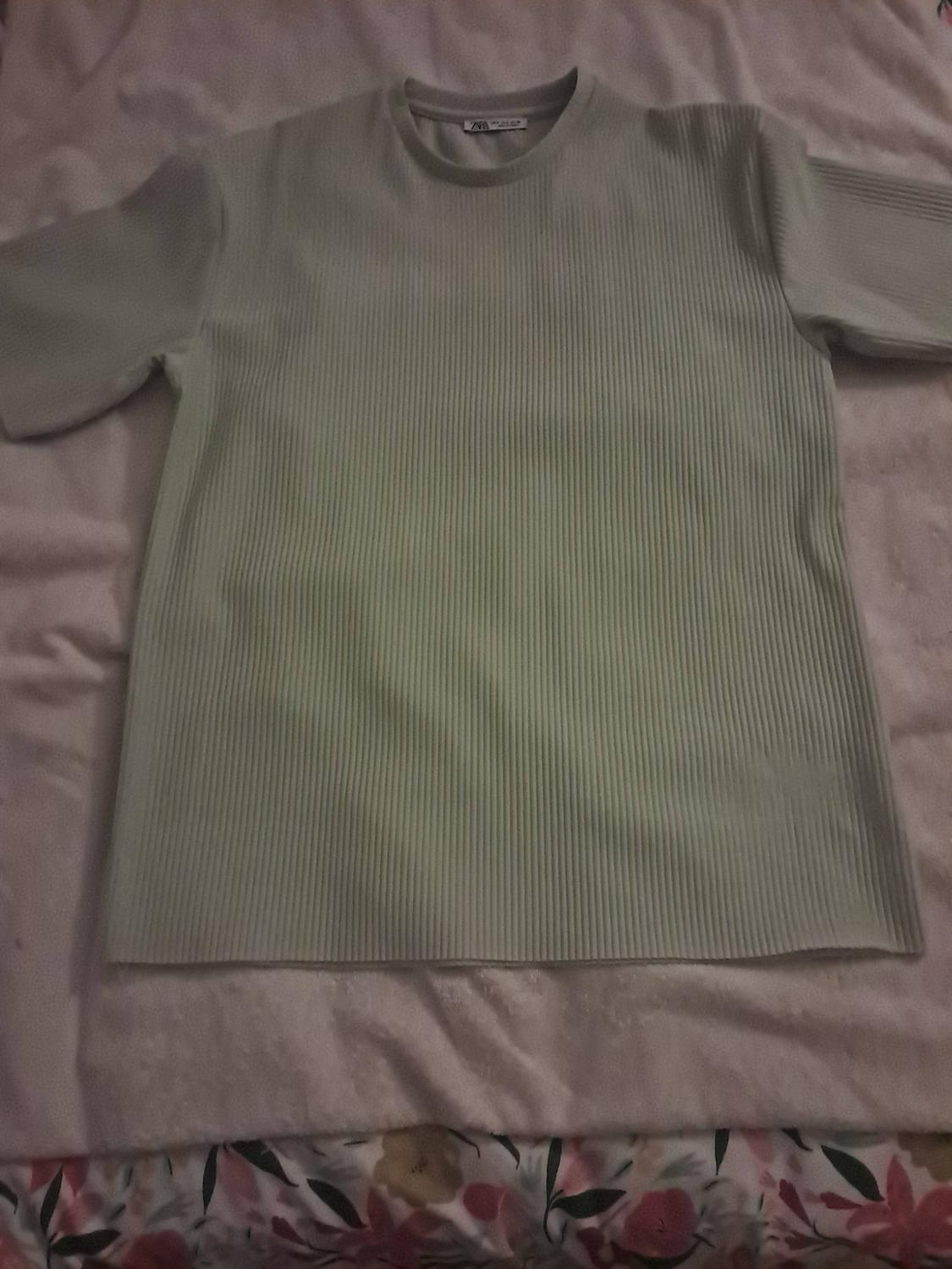 Light green short-sleeved ribbed t-shirt, laid out on a white blanket and floral-patterned sheets.