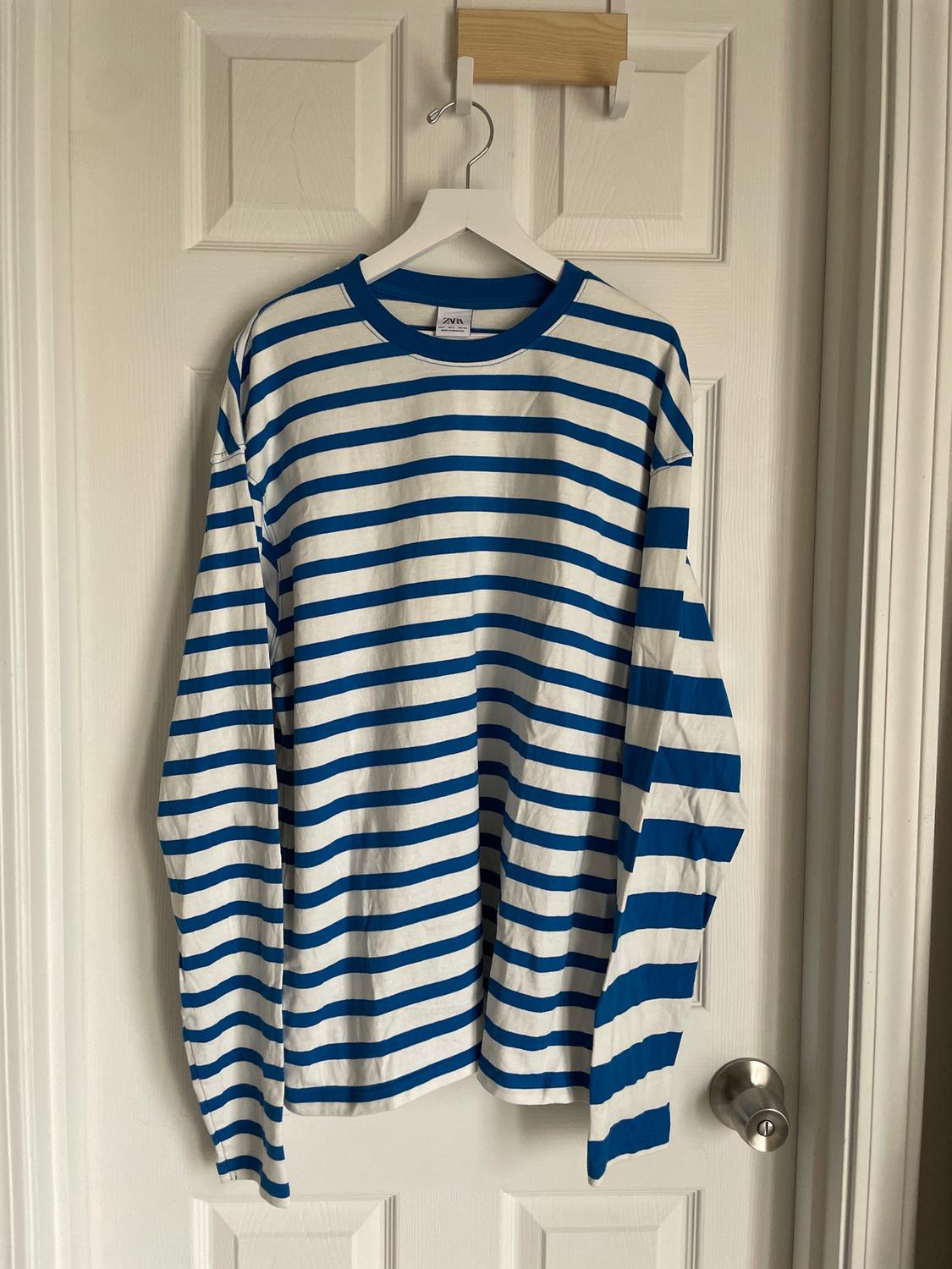 Blue and white striped T-shirt hanging on a white hanger over a white door.