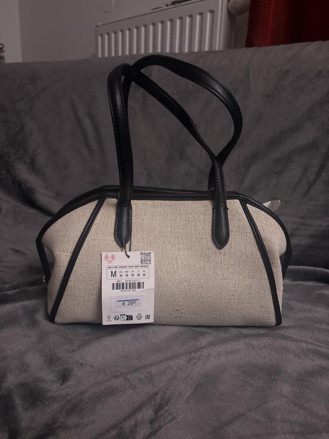 Beige handbag with black piping and handles on a grey blanket. Text: M M M M M M ART.: 6316/710/111 16316710111037 €29.95.