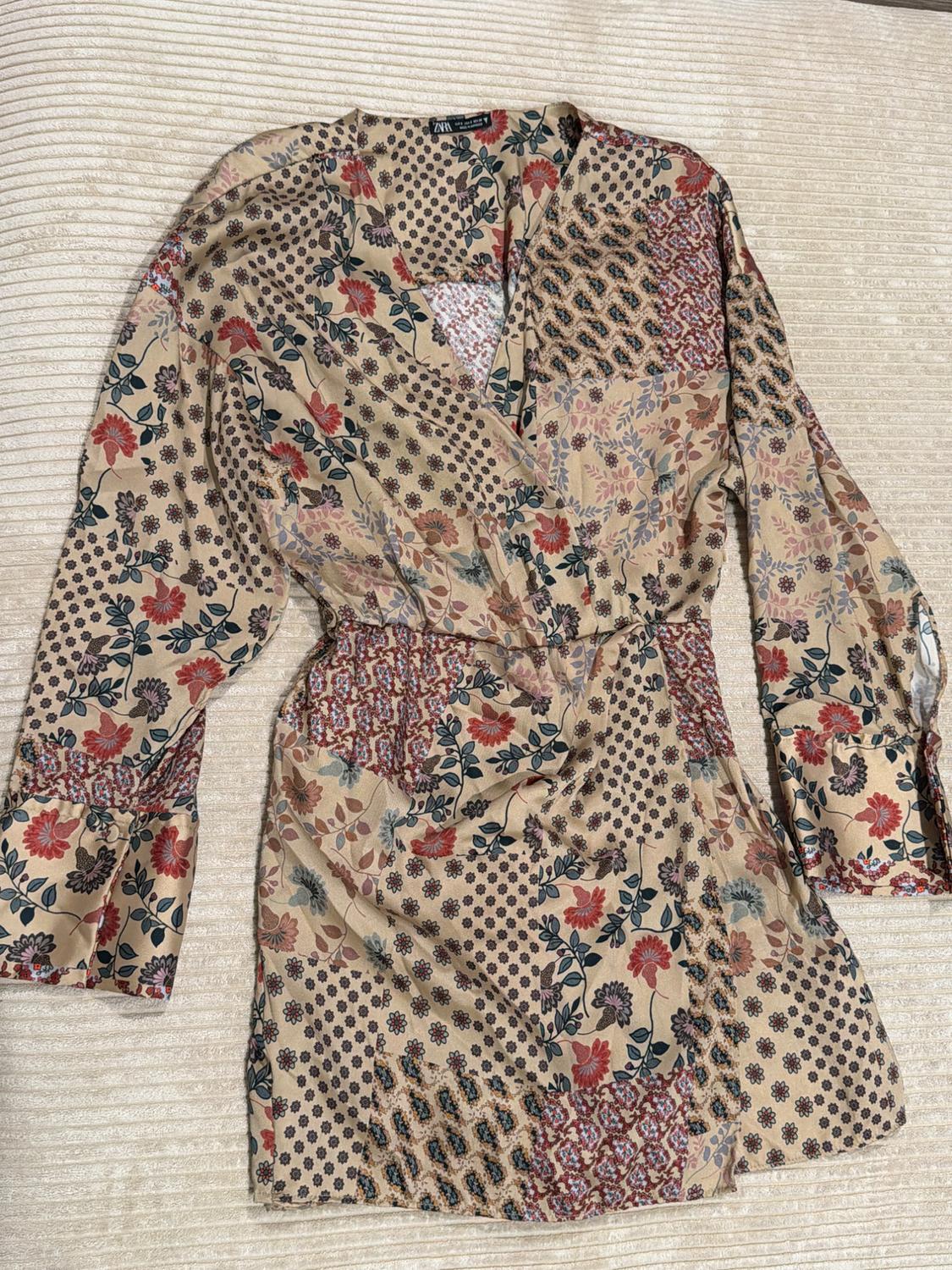 Beige dress with a V-neck, long sleeves, and a floral and geometric print. ZARA label visible. Shown against a textured background.