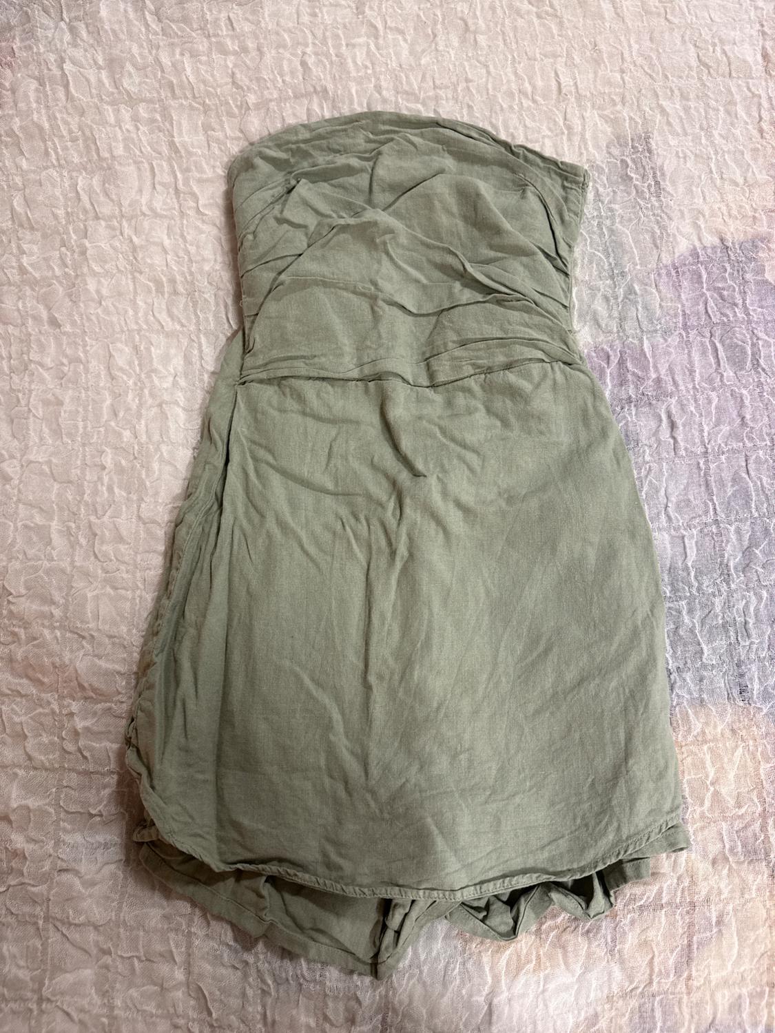 Light green short dress with a strapless neckline and ruched detail, laid out on a light textured fabric. Casual style.