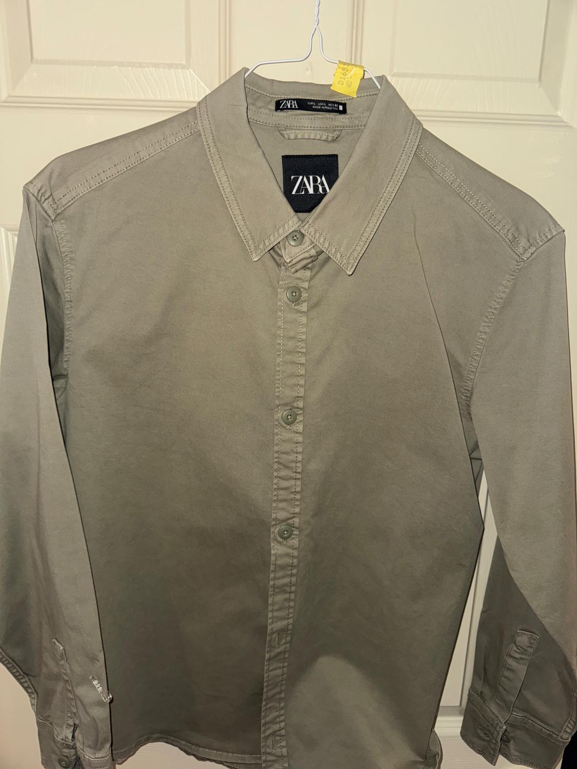 Grey long-sleeved shirt hanging on a hanger, with visible brand label on the collar and white door background.