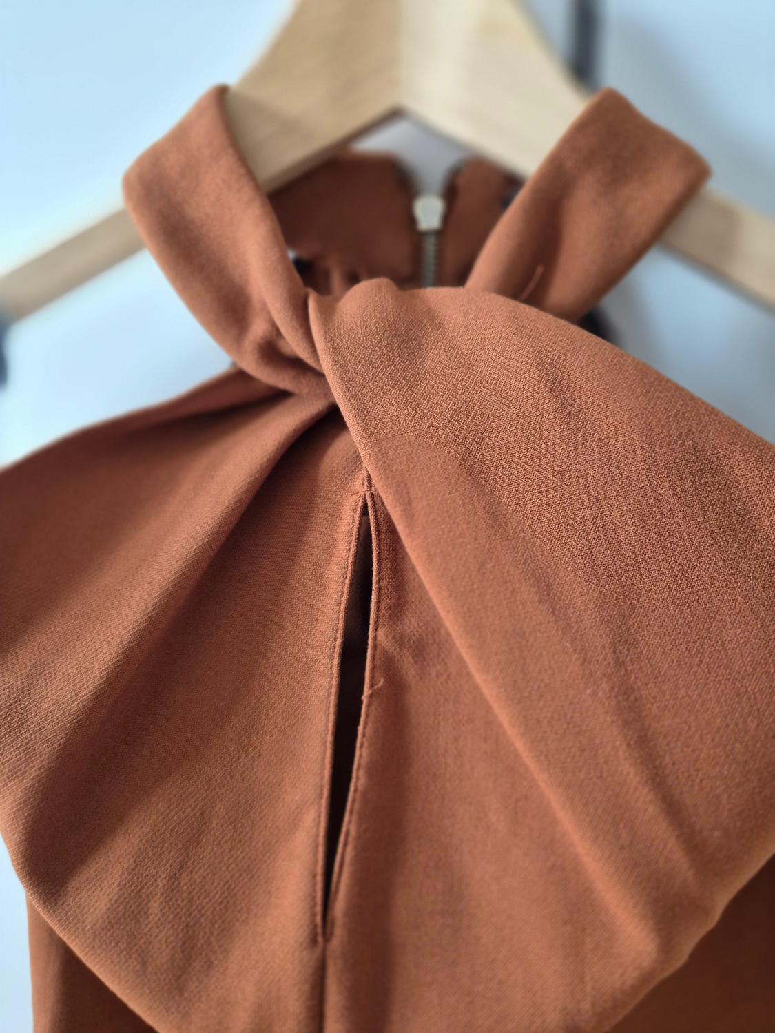 Close-up of a brown dress with a bow on the collar, hanging on a wooden hanger. Blurred background.