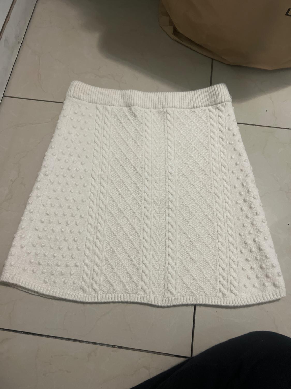 White knitted skirt with cable knit design and dotted texture, placed on a light tiled floor.