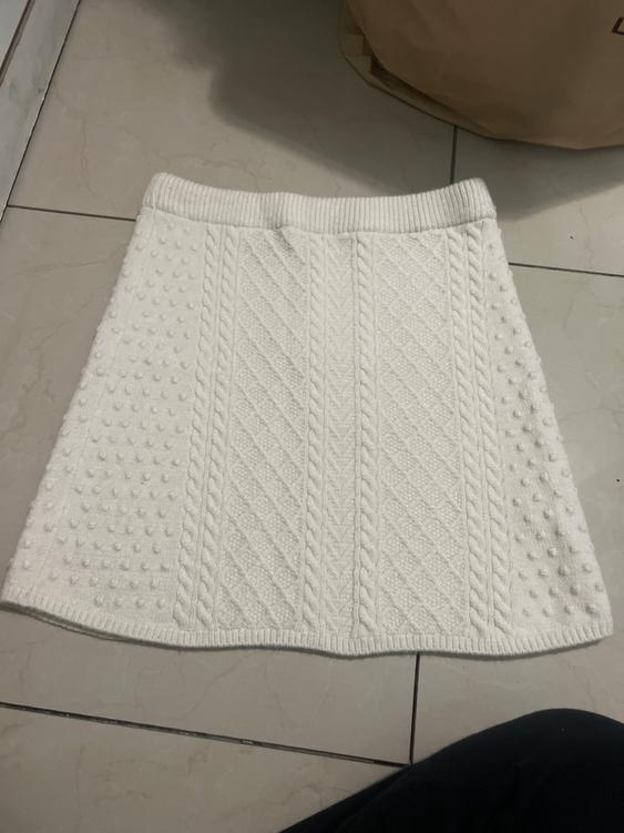 White knit skirt with cable knit design and dot texture, placed on a light tiled floor.