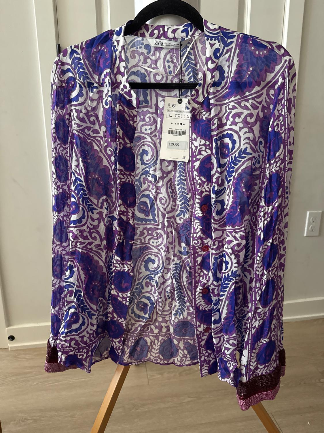 Sheer blouse with purple and blue print, hanging on a black hanger. Visible tag with price of 119.00.
