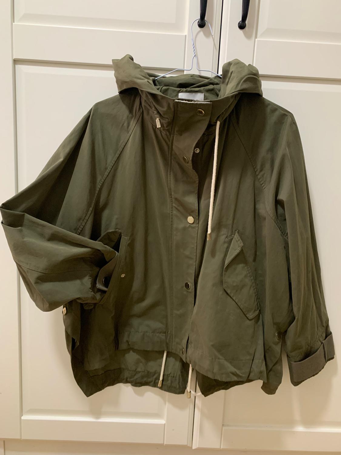 Olive green hooded jacket with drawstrings hanging on a white hanger in front of a white wardrobe.