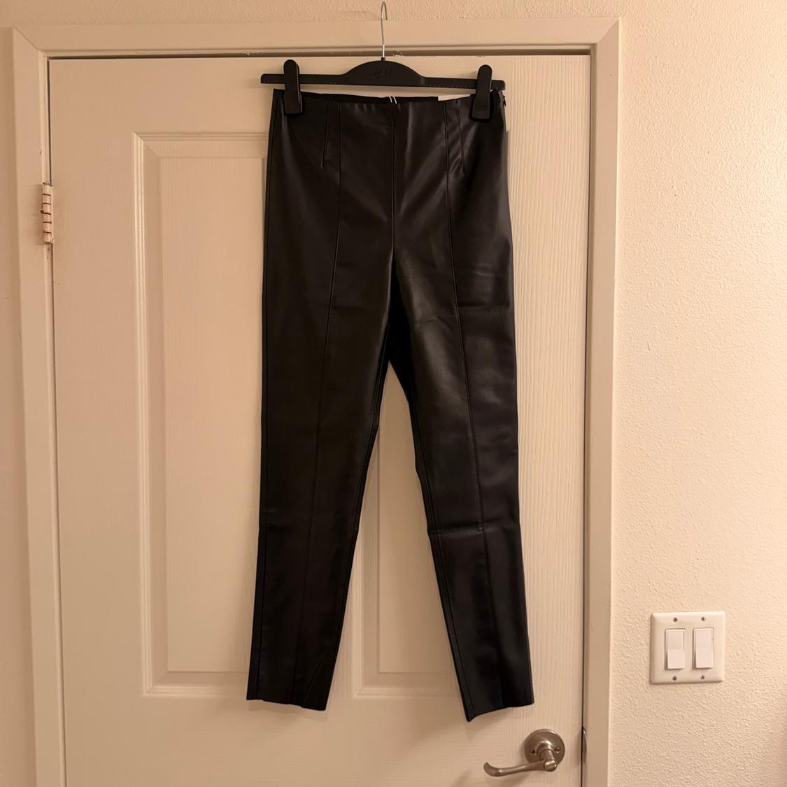Black pants hanging on a hanger over a white door. The warm light highlights the smooth, shiny material of the pants.