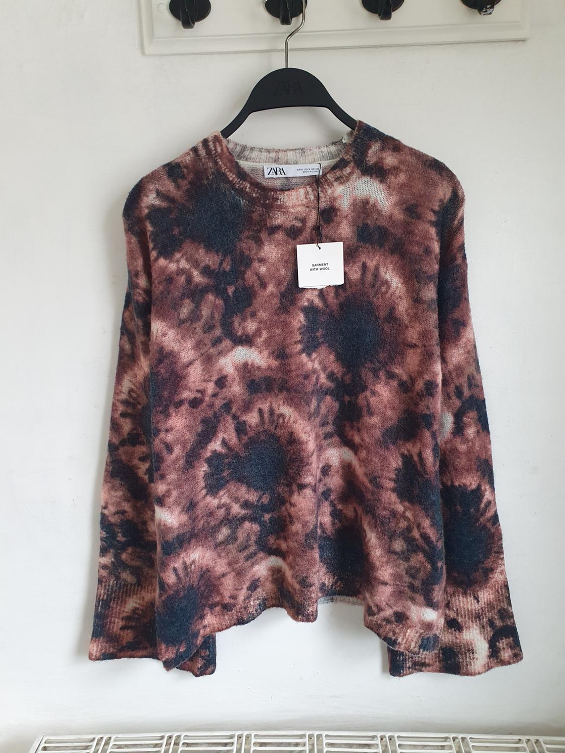 Knitted tie-dye jumper in brown and black tones, hanging on a black hanger with a label that reads "GARMENT DYEING WOOD".