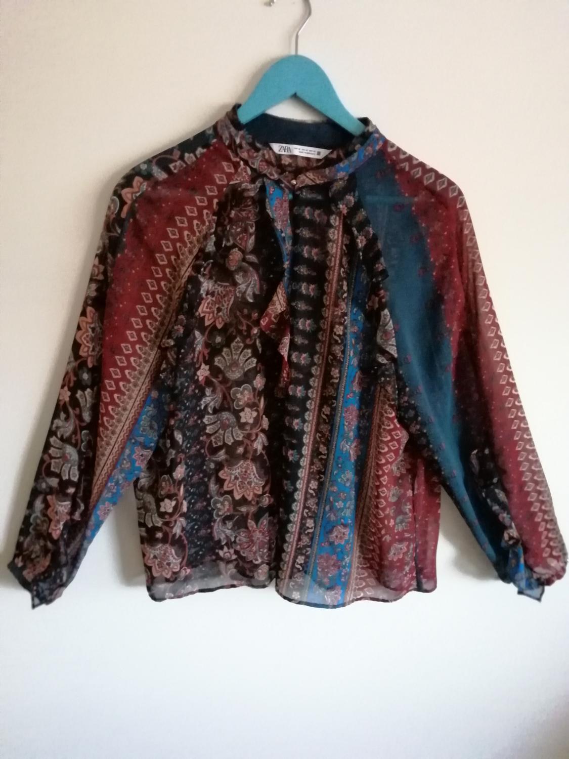 Front view of a printed blouse with ruffles on the chest, long sleeves and a round neck.
