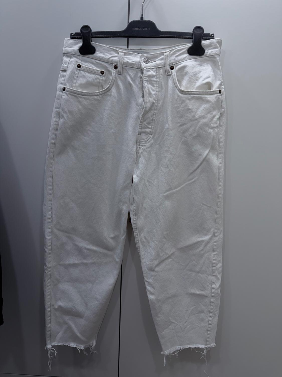 White denim trousers with a frayed hem hanging on a black hanger with the brand "Alberta Ferretti".