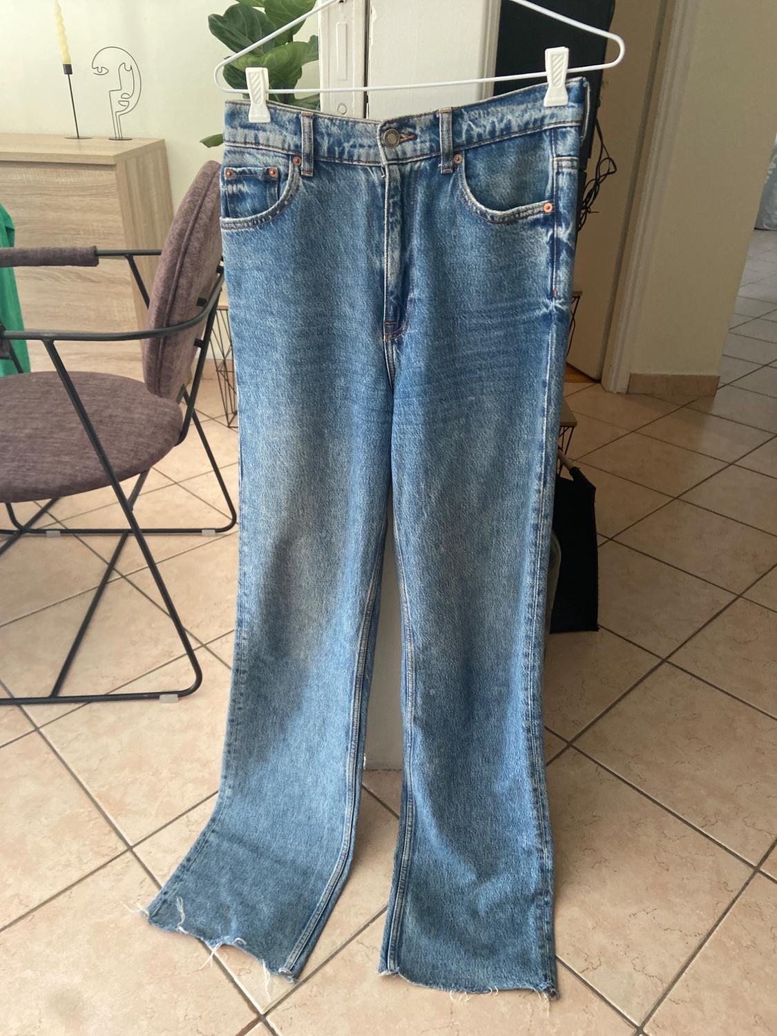 Worn blue jeans hanging on a white hanger in a room with a tiled floor and modern furniture.