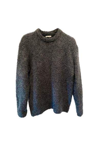Soft-textured grey wool jumper with a round neck and long sleeves, hung against a white background. Label visible on the collar.