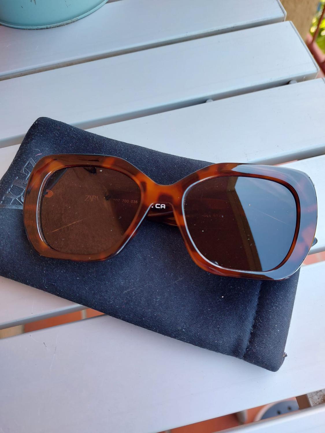 Brown tortoiseshell sunglasses on a black case on a white table. Visible text: "ZARA".