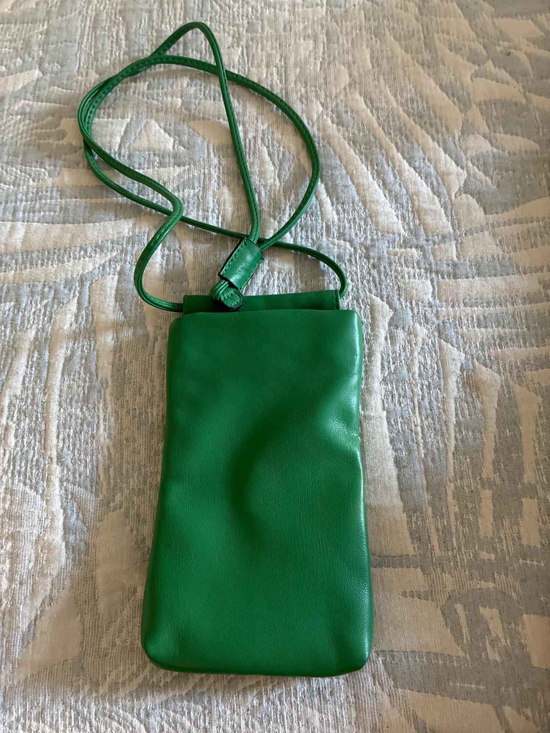 Small rectangular bright green handbag with a thin strap, resting on fabric with a light leaf print.